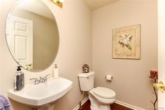 a white toilet sitting next to a bathroom sink under a large round mirror in a bathroom