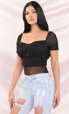 a woman with long black hair wearing ripped jeans and a top that has sheer sleeves