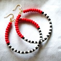 two red and black beaded hoop earrings on white fabric with gold tone hooks,