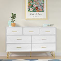 a white dresser with flowers on it in a living room next to a potted plant