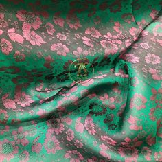 a green and pink flowered fabric with a gold monogram logo on the center