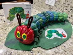 the very hungry caterpillar sits on top of a green leaf next to a book