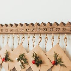 three envelopes are hanging on a wall with pine needles and red berries attached to them