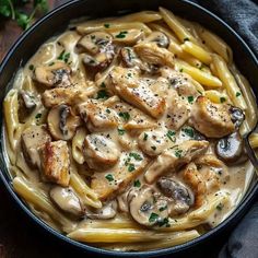 a skillet filled with pasta and chicken covered in mushroom sauce on top of a wooden table