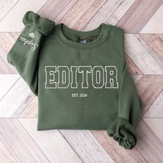 a green sweatshirt with the word editor printed on it, sitting on a wood floor