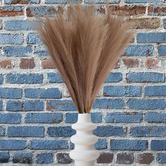 a tall white vase with some brown hair in front of a brick wall and blue bricks