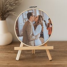 a couple kissing in front of their wedding photo on a wooden easel next to a potted plant