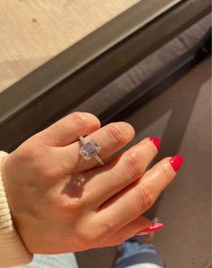 a woman's hand with red nail polish holding an engagement ring in her left hand