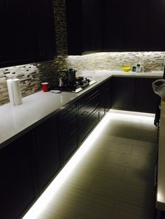 a kitchen with black cabinets and white counter tops is lit up by led lighting under the cabinet lights