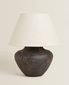 a brown vase with a white shade on it sitting next to a light that is turned on