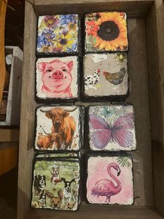 six square coasters with different animals and flowers on them in a wooden box next to a table