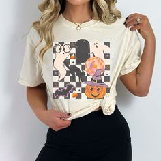 Step into a time warp of Halloween nostalgia with our charming retro-style shirt, carefully crafted on the comfort of a classic Comfort Colors tee. This shirt embodies the spirit of the past while celebrating the spooktacular present. The playful design features a whimsical blend of checkerboard patterns, retro graphics like ghosts, pumpkins, a disco ball, cat, and bat, forming a visual symphony of vintage Halloween elements. With the soothing softness that only Comfort Colors can provide, this shirt becomes more than just a piece of clothing - it's a time-traveling companion that envelops you in comfort while you revel in the delightful retro vibes. Perfect for those who cherish both the past and the magic of Halloween, this shirt combines retro flair with the comfort you adore, making it Retro Halloween T-shirt With Character Print, Retro Halloween Short Sleeve Tops, Retro Halloween T-shirt With Crew Neck, Retro Halloween T-shirt With Screen Print, Retro White Top For Halloween, Retro White Tops For Halloween, Retro Halloween T-shirt Pre-shrunk, Retro Pre-shrunk Halloween T-shirt, Retro Funny Print Halloween Tops