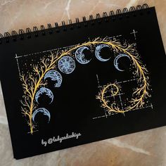 a spiral notebook with the phases of the moon in gold and blue on black paper