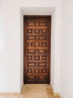 a wooden door in the corner of a white room with tile flooring and beige walls