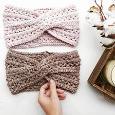 two knitted headbands are shown next to a candle and some cotton flowers