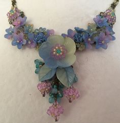 The colors in this necklace are stunning soft hues of blue purple and mint make up this elegant Colleen Toland necklace. The mix of colors give it a periwinkle look. The flowers are hand painted and the entire necklace is beaded with thread and wire. Including the necklace chain itself. This necklace would look great with a pretty summer dress or can be worn casually with even a pair of jeans. Earrings on the model are also available. This is a quality piece of jewelry that will last a life time Blue Bohemian Flower Necklace, Blue Flower-shaped Bohemian Necklace, Blue Bohemian Flower Beaded Necklaces, Bohemian Blue Flower Necklace, Whimsical Blue Beaded Necklaces, Whimsical Handmade Blue Beaded Necklaces, Handmade Whimsical Blue Beaded Necklaces, Jeans Earrings, Pretty Summer Dress