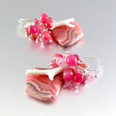 I love these focals! They are Argentine rhodochrosite gems and measure 22x20mm. They have been wrapped in sterling silver wire and dangle below a gorgeous combination of smooth ruby briolettes, pink moonstone, pink sapphire, white branch coral. Each bead is meticulously wrapped onto it's own head pin. The entire cluster is topped. I have used simple sterling ear wires. The earrings measure 1 3/4 (44mm.) from the top of the ear wires. Unique Pink Gemstone Earrings, Sterling Silver Pink Wire Wrapped Earrings, Pink Sterling Silver Wire Wrapped Earrings, Unique Pink Sterling Silver Earrings, White Branches, Black Freshwater Pearls, Pink Moonstone, Peacock Pearl, Handmade Lampwork Bead