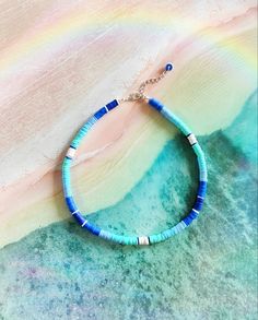 This is The Outer Shore Collection Tidal Blue Beaded Heishi necklace. This boho tropical surf style necklace is inspired by the Choker necklaces that Kiara wore on the Netflix series The Outer Banks. #summer #surfergirl #jewelry #choker #necklace #handmadejewelry #smallbusiness #giftforher Summer Blue Necklaces With Spacer Beads, Blue Spacer Beads Jewelry For The Beach, Bohemian Jewelry With Letter Beads For Beach Season, Blue Beaded Necklace With Spacer Beads For Summer, Blue Beaded Necklaces With Spacer Beads For Summer, Blue Bohemian Heishi Beads Jewelry, Blue Beaded Beachy Jewelry, Blue Single Strand Beaded Necklace For Summer, Blue Strand Necklaces For Beach Season