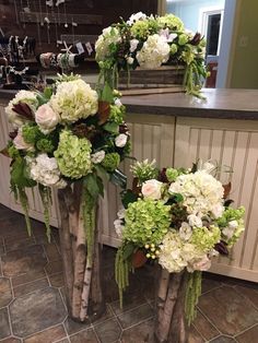 two vases filled with white and green flowers on top of a stone floor next to a counter