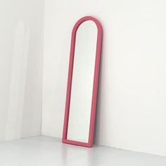 a pink mirror sitting on top of a white wall next to a red floor lamp