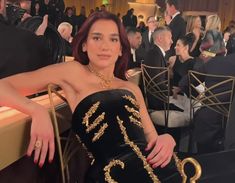 a woman in a black and gold dress sitting on a chair at a formal event