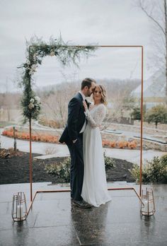 a bride and groom standing in front of an outdoor ceremony arch