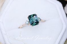 a fancy ring with an emerald colored stone surrounded by three white diamonds on a cushion