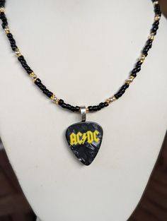 a necklace with a guitar pick and ac / dc logo is displayed on a mannequin