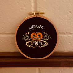 a black and orange embroidered pumpkin with the words football on it, sitting on a wooden shelf