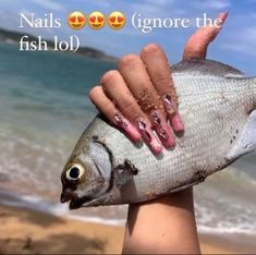 a person holding up a fish on the beach with their fingers painted pink and yellow