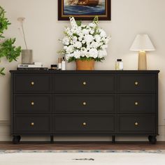 a black dresser with white flowers on top and a painting in the corner above it