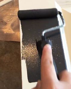 a hand is holding a paint roller and painting the wall with black paint on it