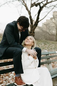 a man and woman sitting on top of a wooden bench in front of a tree