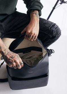 a man with tattoos sitting on top of a black bag and holding his hand in the pocket