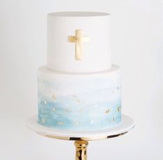 a white and blue cake with a gold cross on top is sitting on a stand