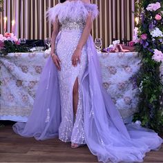 a woman standing in front of a table wearing a purple dress with feathers on it