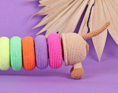 a crocheted caterpillar sits in front of a palm leaf and purple background