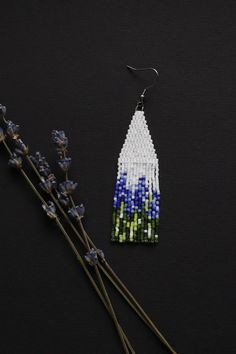 a pair of beaded earrings sitting next to some lavenders on a black surface