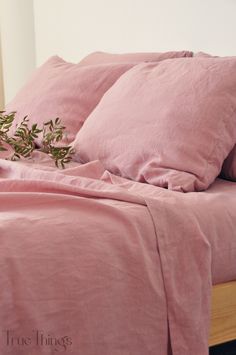 a bed covered in pink sheets and pillows with a plant on top of the pillow