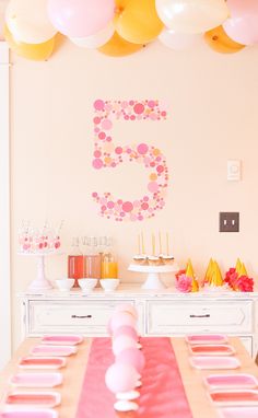 the table is set up for a birthday party with pink, yellow and white balloons