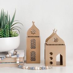 two small wooden buildings sitting on top of a table next to a potted plant