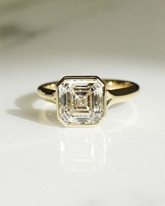 an engagement ring with a square cut diamond in the center, on a white surface