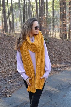 a woman is wearing a yellow scarf and black pants while standing in front of some trees