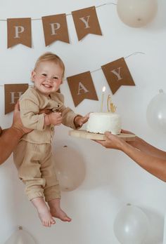 a baby is being held up by two adults while holding a birthday cake with candles