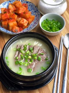 a bowl of soup with meat and green onions in it next to some chopsticks