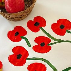 an apple and some red flowers on a white table with apples in the back ground