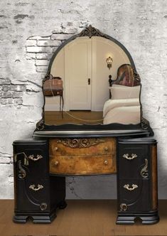 an old fashioned vanity with a mirror on the top, and a bed in the background