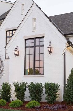 a white house with black windows and plants in the front yard, on a cloudy day