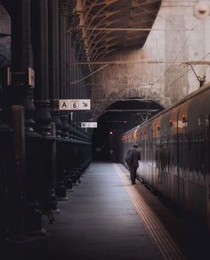 a man standing next to a train on the tracks at a station with no people