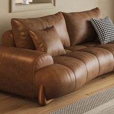 a brown leather couch sitting on top of a hard wood floor next to a window